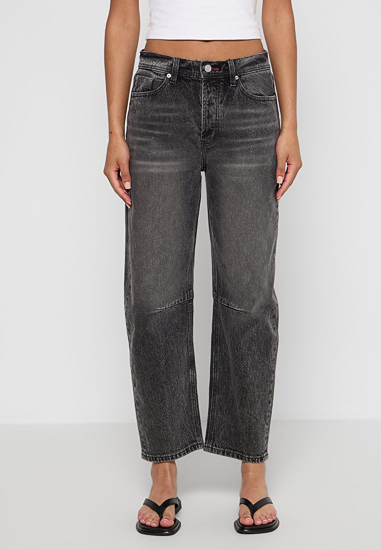 Jeans a vita alta di un grigio scuro con ampie gambe, con leggeri sbiadimenti, cinque tasche e chiusura con bottone. Abbinati a un crop top bianco aderente e sandali neri.