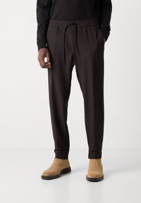 Pantaloni jogger tapered de culoare maro închis, cu talie elastică și șnur de ajustare, având buzunare laterale și manșete cu nervuri la glezne, confecționați dintr-un material fin.