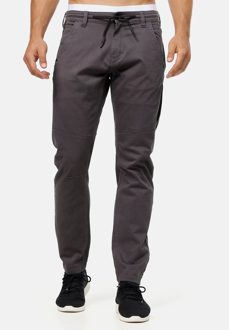 Pantalones ligeros grises con cintura con cordón, diseño ajustado y paneles en las rodillas, combinados con zapatillas deportivas negras.