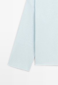 Lyseblå langærmet sweatersektion, der viser glat strikket stof og lige kant på lys baggrund.