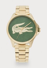 Goldtone-Uhr mit grünem Zifferblatt, das ein Krokodil-Design zeigt. Armband aus rostfreiem Stahl mit Gliederdekoration. Einfache Stunden- und Minutenzeiger.