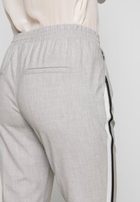 Grijze op maat gemaakte broek met een elastische tailleband, voorzien van zijstrepen in zwart en wit, en een achterzak aan de rechterkant.