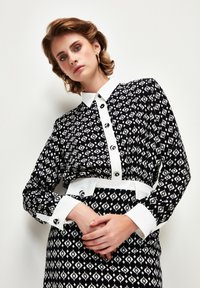 Black and white patterned dress with a collared neckline, button front, and a white belt. The fabric has a geometric design and smooth texture.