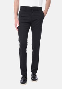 I pantaloni in cotone neri presentano un design a gamba dritta con tasche frontali e chiusura a bottone, abbinati a scarpe nere per il contrasto.