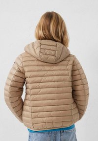 Beige donsjack met horizontale stiksels, een capuchon en een aansluitend ontwerp. Gestructureerde stof met een lichte glans, gecombineerd met een blauw hemd eronder.