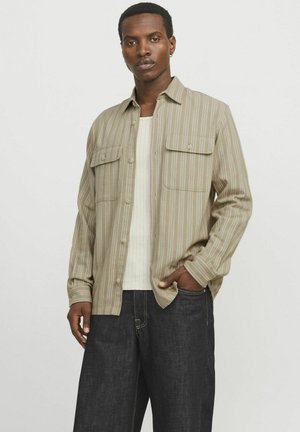 Beige and cream striped shirt with two chest pockets, button-down front, and long sleeves, paired with dark denim jeans.