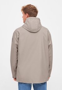 Light beige waterproof jacket with a hood, sleek design, smooth texture, and featureless back. Adjustable cuffs and minimal branding detail.
