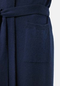 Mörkblå stickad morgonrock med bälte, med en framficka och en strukturerad tyg. Designen har ett mjukt, varmt utseende.