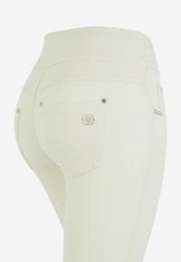 Jeans bianchi a vita alta realizzati in tessuto elasticizzato; presentano due tasche posteriori con hardware argentato e borchie decorative vicino ai bordi delle tasche.