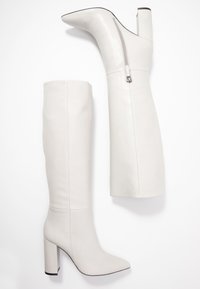 Botas de cuero blancas hasta la rodilla con punta afilada, tacón bloque y cremallera lateral. Textura suave con un brillo sutil y suela negra contrastante.
