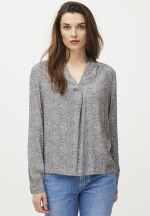 Blusa grigia a maniche lunghe con un motivo geometrico bianco, design a scollo a V e una vestibilità comoda, abbinata a jeans in denim blu.