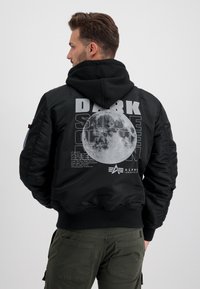 Giubbotto bomber nero con cappuccio, dotato di una grande grafica della luna e testo "LATO OSCURO DELLA LUNA" sul retro, polsini e orlo a costine.