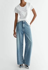 White short-sleeve t-shirt with a heart graphic and silver accents, paired with light blue wide-leg jeans and shiny silver high heels.