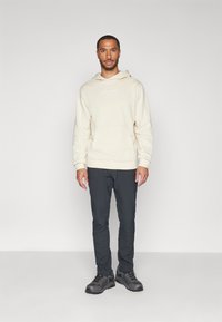 Beżowa bluza z kapturem z przednią kieszenią, połączona z ciemnymi spodniami i czarnym obuwiem z wytrzymałą podeszwą. Prosty design z minimalnym oznakowaniem.