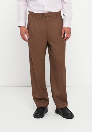 Pantalons marron sur mesure avec une coupe droite, dotés de deux plis avant et d'une fermeture à bouton, associés à des chaussures noires sur un fond blanc.