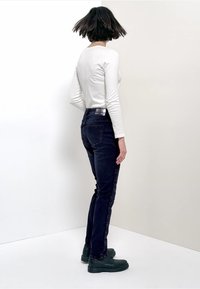 Slim-fit tummansiniset farkut, joissa takataskut, korkea vyötärö ja näkyvät saumat. Yhdistetty vartalonmyötäiseen valkoiseen pitkähihainen puseroon ja mustiin saappaisiin.