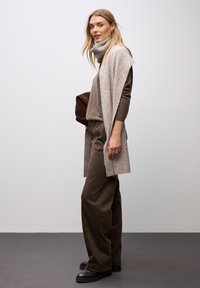 Pull en tricot marron avec un pantalon assorti ; cardigan ouvert léger marron clair en superposition ; bottines noires ; sac marron lisse. Tenue simple et cohérente.