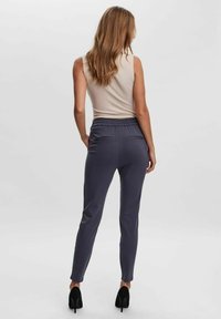 Mörkgrå tapered byxor med en slät textur, elastisk midja och två bakfickor, tillsammans med en ljusbeige ärmlös topp.