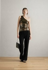 Metalická zlatá jednobodová top se šperky, v kombinaci s černými kalhotami a stříbrnými mokasíny; model drží černou kabelku s řetízkem.