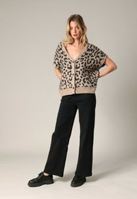 Cardigan beige à imprimé léopard avec des manches courtes et un col en V, associé à un pantalon noir à jambes larges et des chaussures noires à lacets. Textures simples.