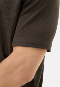 Short-sleeved brown top with textured pattern, crew neck, and a smooth finish; fabric appears lightweight and breathable.