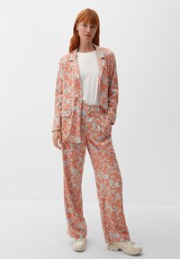 Abito floreale in corallo e azzurro chiaro, composto da un blazer e pantaloni a gamba larga. Il tessuto ha una texture morbida con una leggera lucentezza.