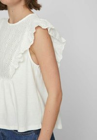 Top blanco con detalle de broderie anglaise en la parte frontal y mangas con volantes. Corte relajado con escote redondo.
