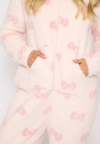 Weicher rosa Fleece-Overall mit hellrosa Schleifenmustern, Kapuze und vorderen Taschen. Verfügt über einen Reißverschluss und einen strukturierten Stoff.