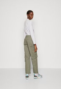 Cargo pants in olive green fabric with side pockets, paired with a light purple oversized sweater. Model wears multicolored sneakers.