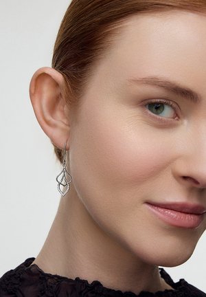 Srebrne kolczyki wiszące z warstwowym wzorem w kształcie łzy i małymi akcentami z kamieni, zawieszone na haczyku. Wykończenie o delikatnym połysku.