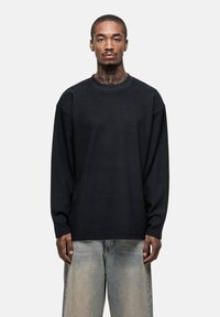 Schwarzes Langarmshirt mit gerippter Textur, ausgestattet mit Rundhalsausschnitt und lockerer Passform, kombiniert mit hellblauen, weiten Jeans.