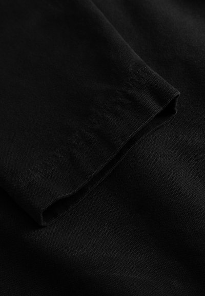 Tissu noir à texture lisse, présentant un bord de manche plié et un détail de couture propre et sans ornement.