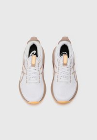 Weiße Sportschuhe mit einer strukturierten Oberseite, hellbraunen Akzenten und flachen Schnürsenkeln. Sie verfügen über einen weichen Kragen und ein sichtbares Markenlogo auf der Innensohle.