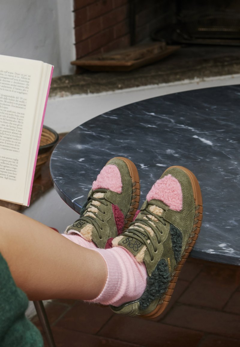 Wildlederschuhe in olivgrün und rosa mit flauschigen Akzenten, Gummisohle und Schnürsenkeln. Getragen mit hellrosa Socken, die auf einem Marmor Tisch liegen.
