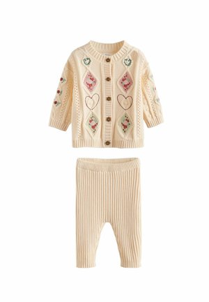 Strickjacke für Babys in Creme mit dekorativer Diamant- und Herzstickerei, ausgestattet mit Holzknöpfen. Ribbestrick-Leggings in Creme ergänzen das Set.