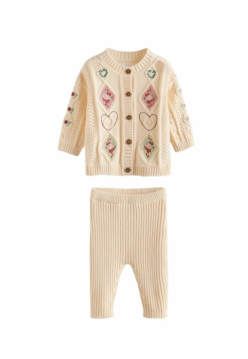Strikket babykardigan i creme med dekorative diamant- og hjertebroderier, der har træknapper. Ribbestrikkede creme leggings komplementerer sættet.