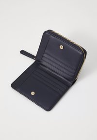 Navy leather wallet with a zip closure, gold hardware, multiple card slots, a press stud, and "Tommy Hilfiger" embossed on the interior.