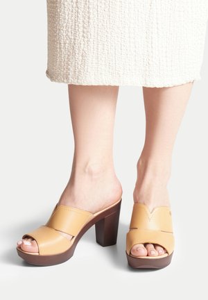 Offene High-Heels aus hellbraunem Leder mit glatter Oberfläche, ausgestattet mit einem breiten Riemen, einem V-förmigen Design und einer klobigen braunen Sohle.