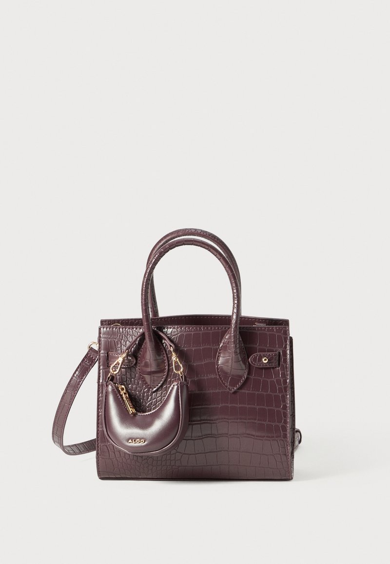 Sac à main violet foncé à texture crocodile avec deux anses, une petite pochette attachée et une bandoulière amovible sur un fond clair.