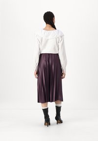 Blusa bianca con colletto rotondo e arricciato e maniche lunghe. Abbinata a una gonna midi plissettata viola e stivali neri con tacco.