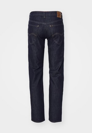 Jean en denim bleu foncé vu de dos avec deux poches arrière, coutures contrastées et un patch en cuir marron sur la ceinture.