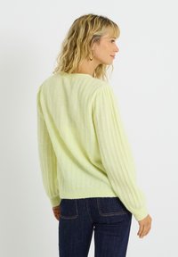 Suéter de punto amarillo claro con textura acanalada, mangas largas abullonadas y escote redondeado, combinado con jeans de mezclilla oscura.