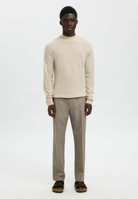 Pull en tricot beige à manches longues associé à un pantalon ajusté marron clair et des sandales noires, offrant une coupe décontractée et une texture douce.