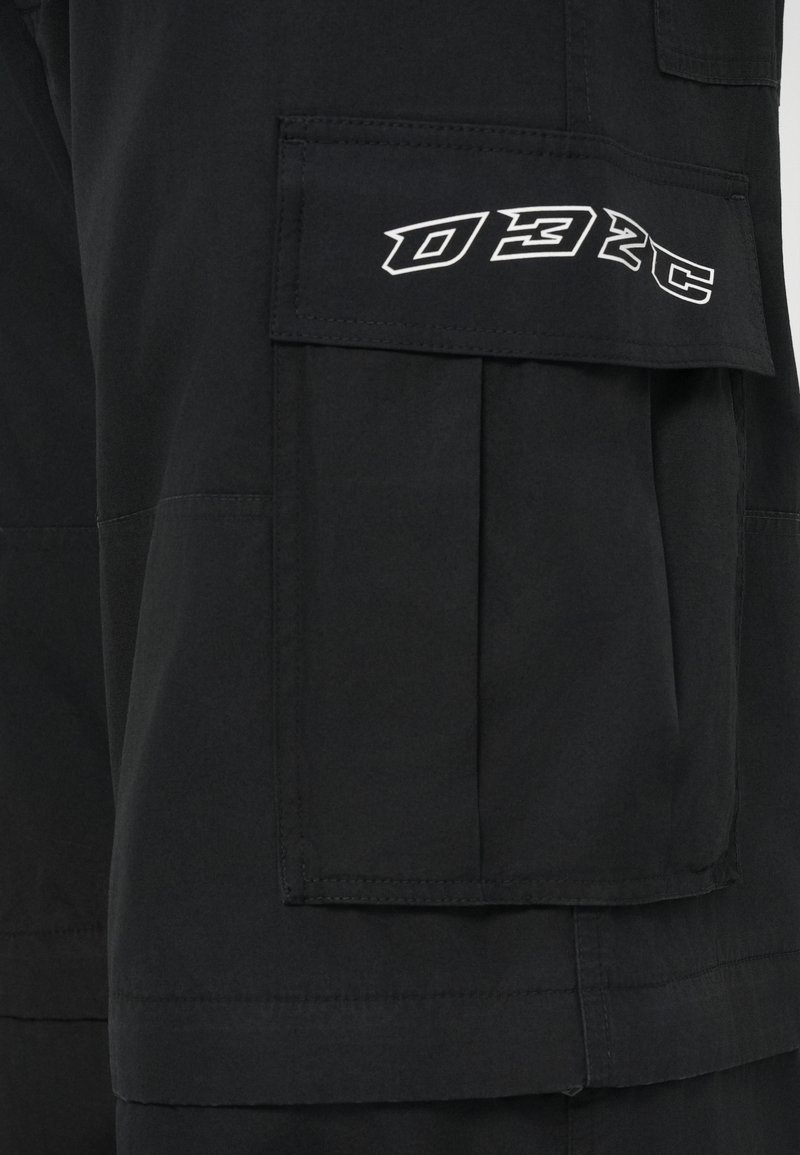 Schwarze Cargo-Shorts aus strukturiertem Stoff, mit einer großen Seitentasche und einem weißen "032C"-Logo auf der Taschenklappe.