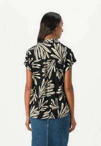 Zwarte shirt met korte mouwen, versierd met een beige bladpatroon en een rugplooitje. Gecombineerd met een denim rok.