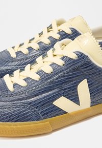 Ζευγάρι μπλε sneakers με υφή, με κρέμ κορδόνια, γλώσσα και λογότυπο, που διαθέτουν σόλα από καουτσούκ καραμέλας και ραμμένα λεπτομέρειες.