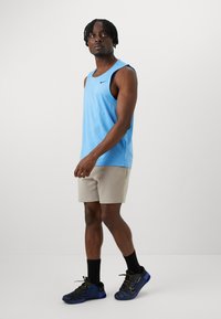 Hellblaues ärmelloses Tanktop, beiges Shorts, schwarze Socken und schwarze/blaue Nike-Sneaker. Glatter Stoff mit minimalistischem Design und Logo.