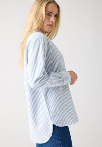 Light blue and white striped long-sleeve shirt with a rounded hem and buttoned cuffs, made from a woven fabric, features a relaxed fit.