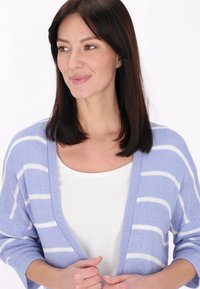 Világoslila kardigán fehér csíkokkal, nyitott elülső résszel és háromnegyed hosszú ujjal. Puha tapintás és laza fazon. Fehér blúz alatta.