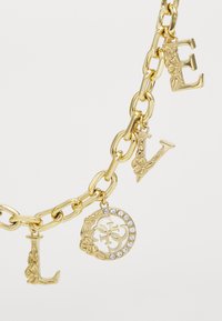 Gouden kettingarmband met gegraveerde lettercharms die "LIEFDE" spellen, met een ronde hanger met rhinestones en bloemaccenten.